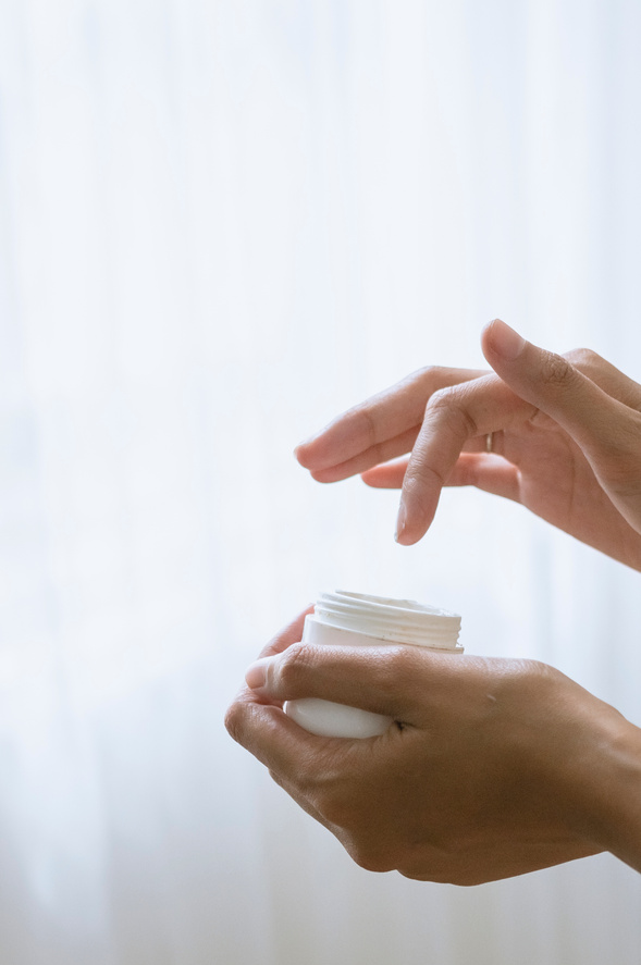Hands with a Small Container of Cream on White Background